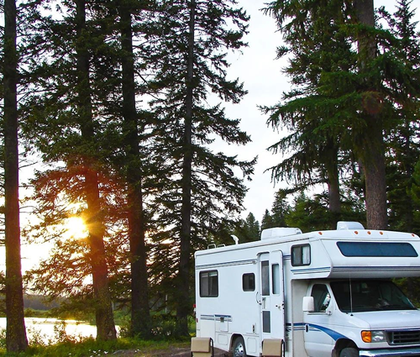 Camper parked in trees near lake with sunset