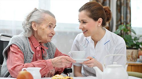 A nurse is serving an elderly woman a cup of tea.