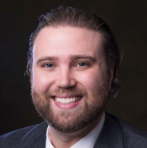 Man with light skin and beard, wearing a suit, smiling.