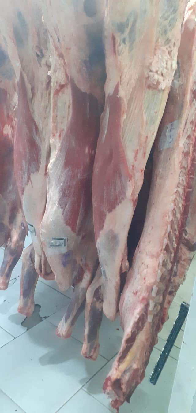Canales de carne colgadas en una carnicería, mostrando cortes de carne de res, con carne roja y hueso visibles.