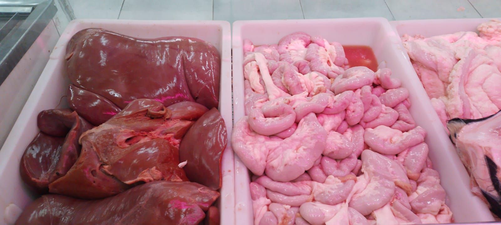 Tres bandejas blancas de carne cruda en una carnicería: hígado, intestinos y otros cortes.