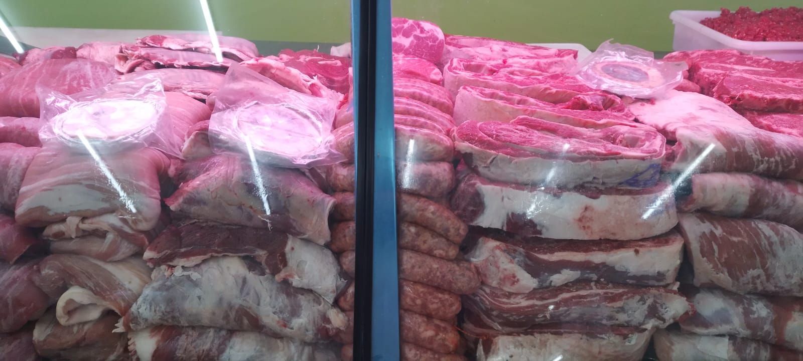 Exhibición de carne cruda, incluyendo tocino y salchichas, en una vitrina refrigerada de carnicería.
