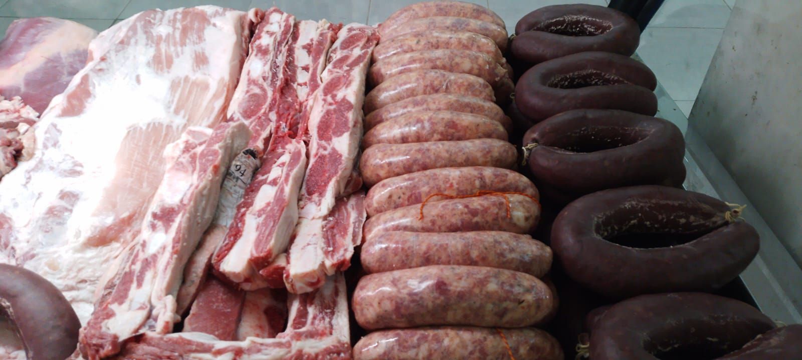 Exhibición de diversas carnes crudas, incluyendo costillas, salchichas y morcillas.