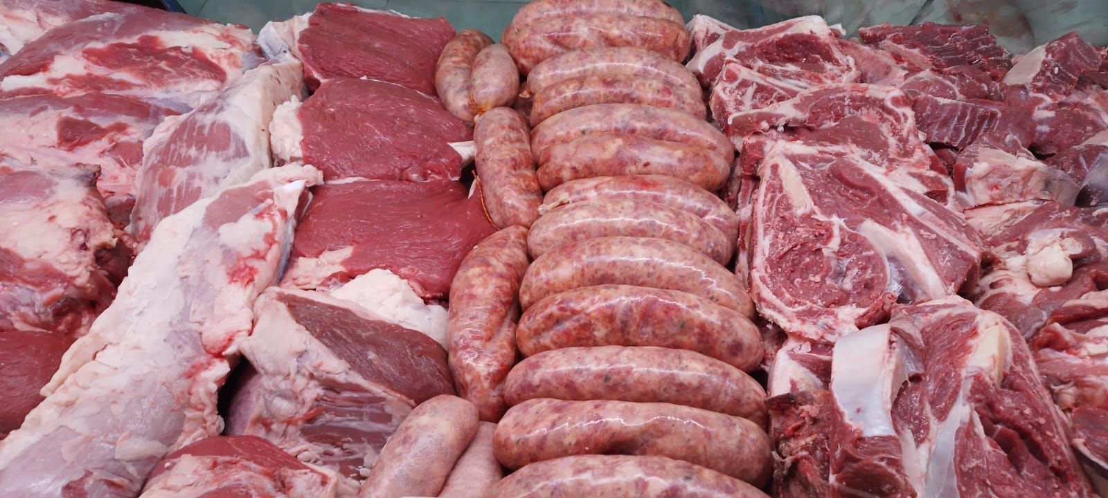 Diversos cortes de carne cruda, incluyendo salchichas y filetes, expuestos en una carnicería.