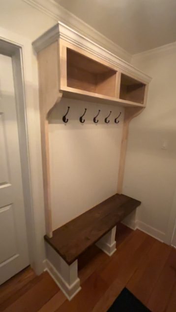 Built-in mudroom nook with hooks, upper cubbies, and a dark wooden bench against white walls.