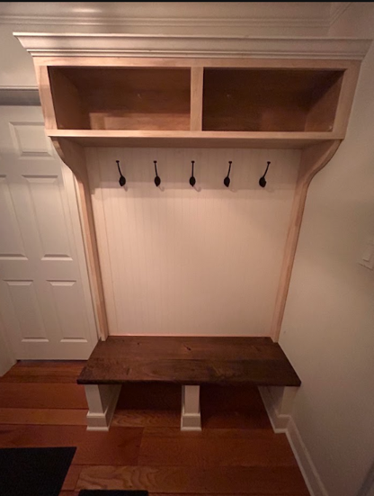 Built-in entryway bench with hooks and cubbies, finished in light wood and white walls.