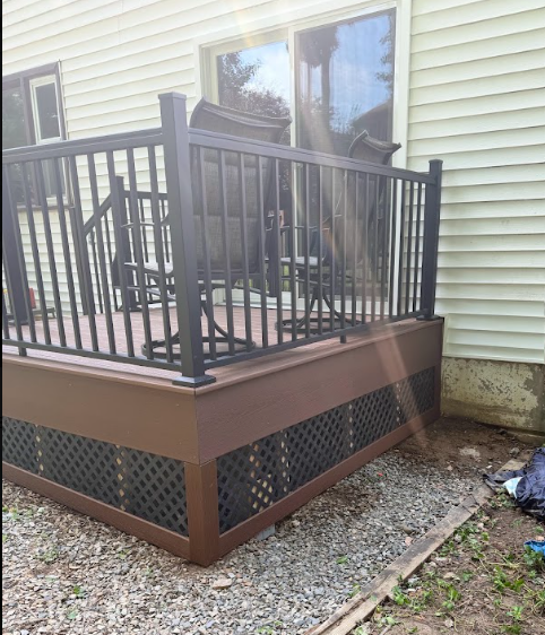 Small backyard deck with black railing, brown trim, and gravel beside a house.