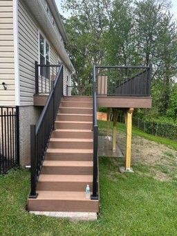 Exterior stairs with black railings leading to a raised deck beside a house.