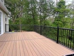 Wooden deck with black railing overlooking a green backyard and trees.