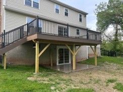 Two-story house with an elevated deck and stairs over a ground-level patio area.