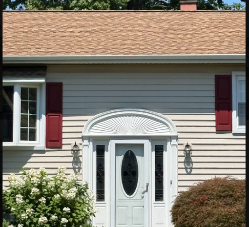 Front entrance of a house with white door, red shutters, beige siding, and flower shrubs.