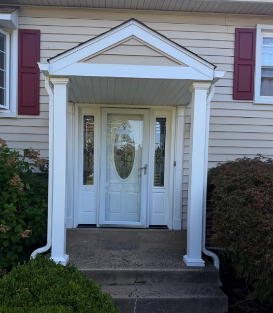 Front porch entrance with white columns, a glass front door, and red shutters on a house.