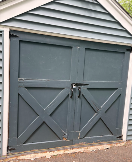 Closed gray double garage doors on a small shed with white trim and an X-brace design.