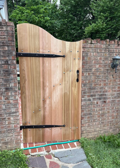 Wooden garden gate set in a brick wall, with black hinges and handle.