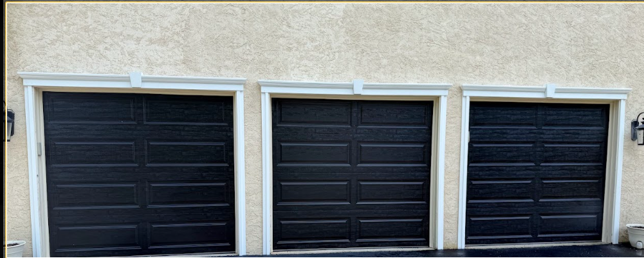 Three black garage doors set in a beige stucco wall with white trim.