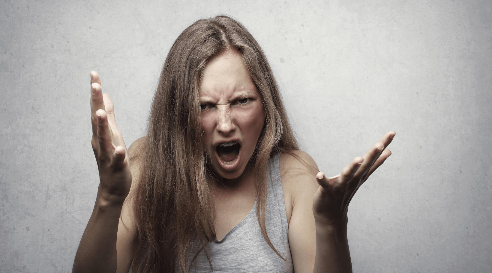 A woman is screaming with her mouth open and her hands in the air.