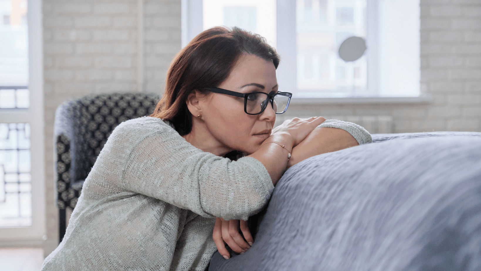 A woman wearing glasses is leaning on a couch.