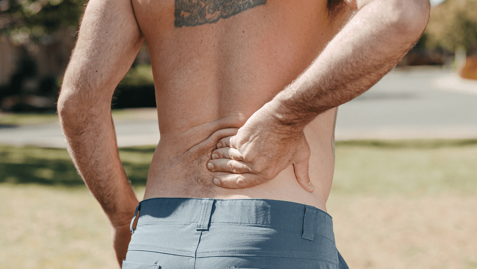A shirtless man is holding his back in pain.