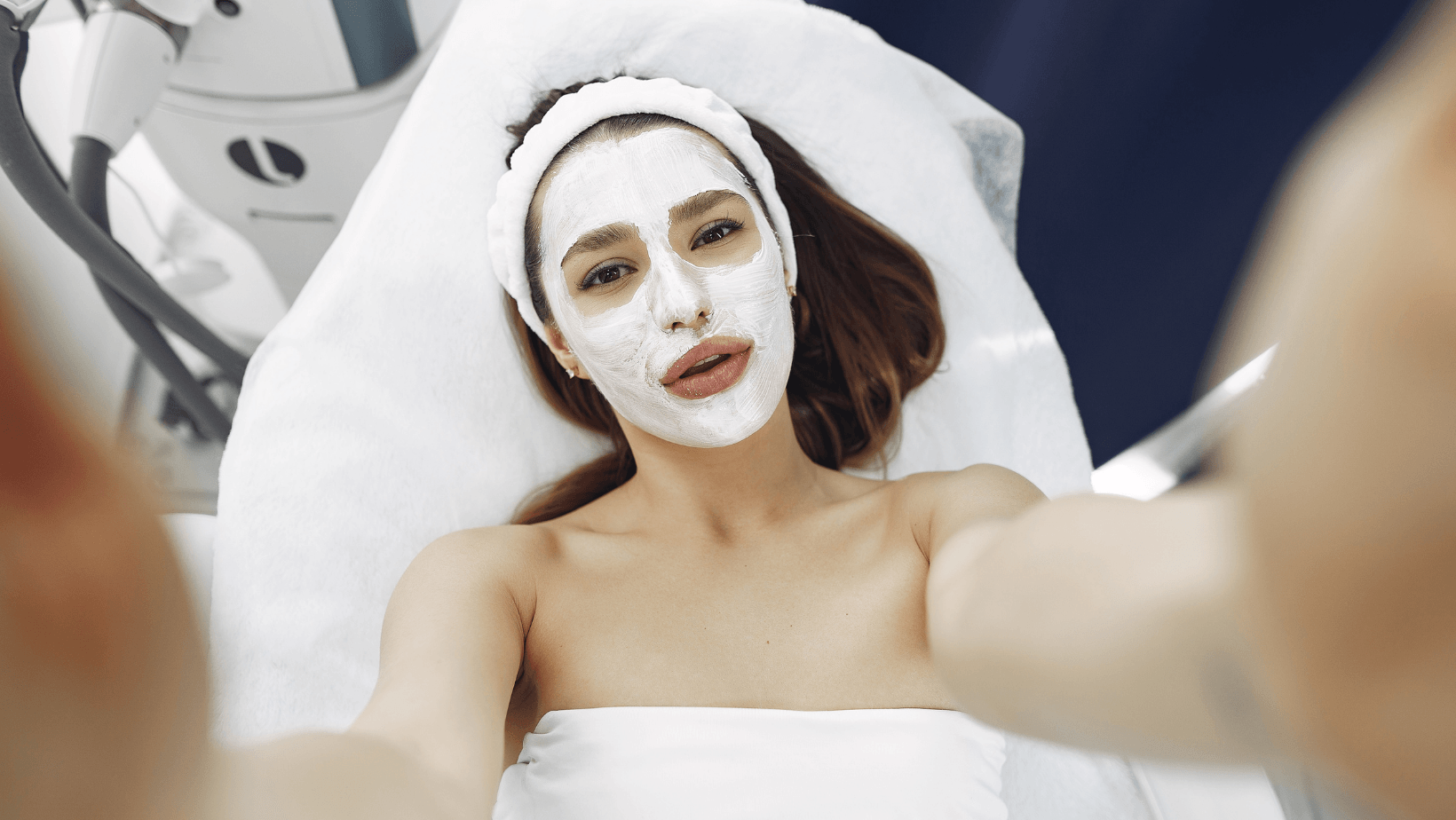 A woman is taking a selfie with a white mask on her face.