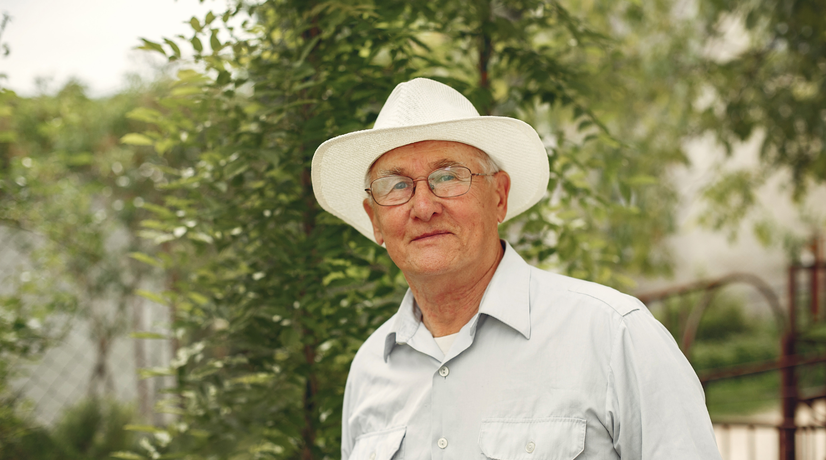 A man wearing a cowboy hat and glasses is standing in front of a tree.