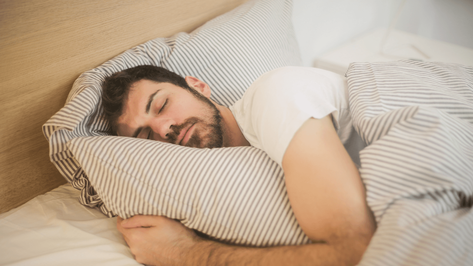 A man is sleeping in a bed with striped sheets and pillows.