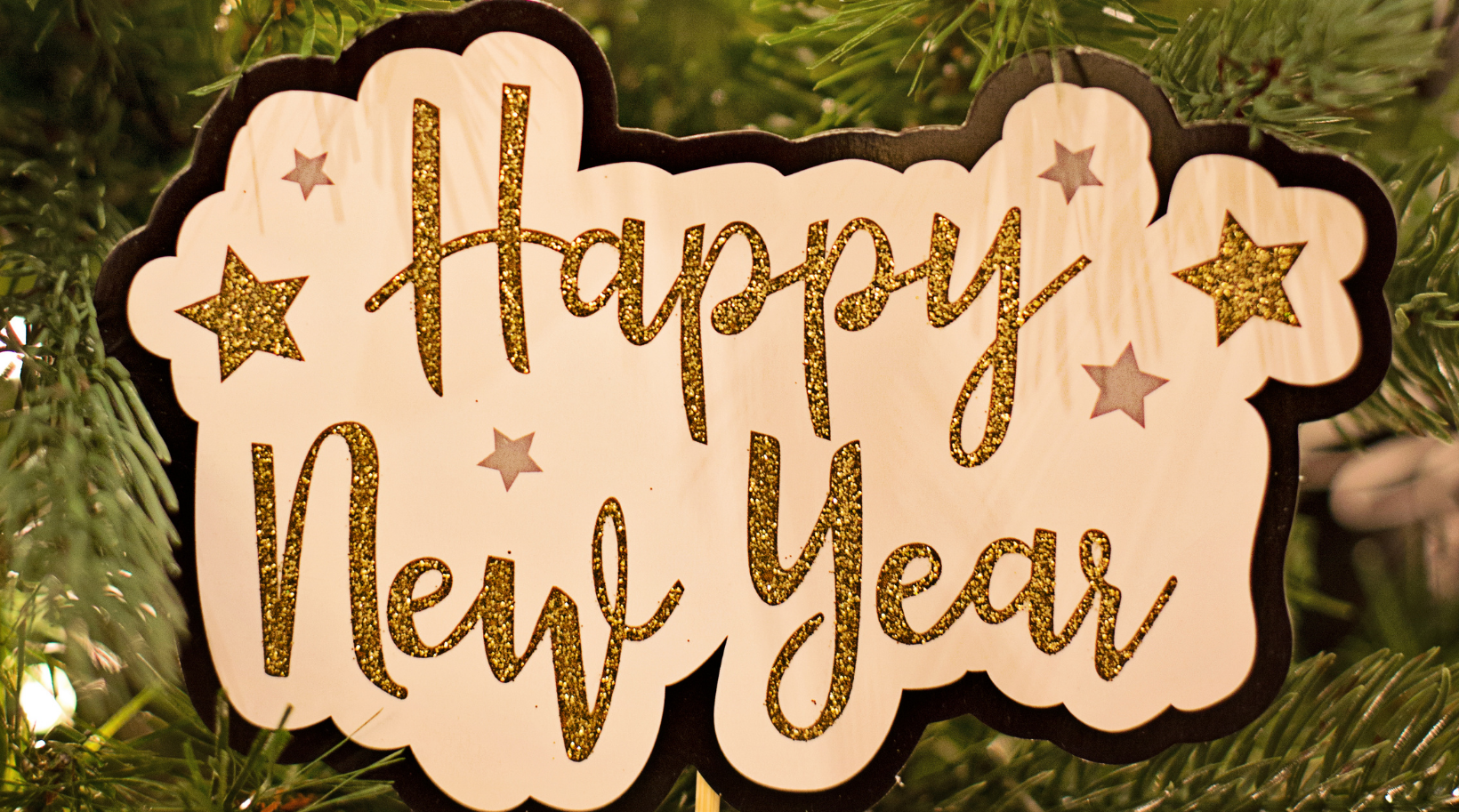 A happy new year sign is hanging on a christmas tree.