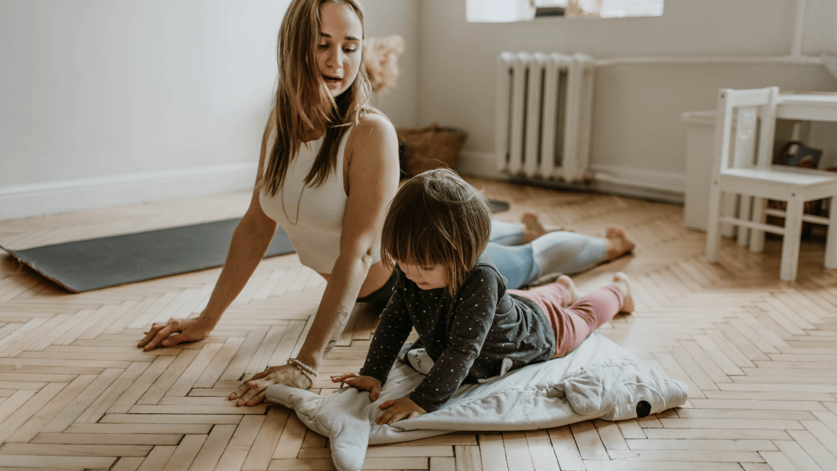 A woman and a child are doing yoga on a wooden floor.