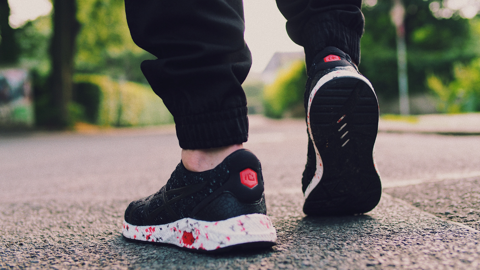 A person wearing a pair of black and white sneakers is walking down a street.