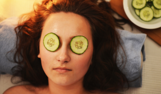 A woman is laying on a towel with cucumber slices on her eyes.