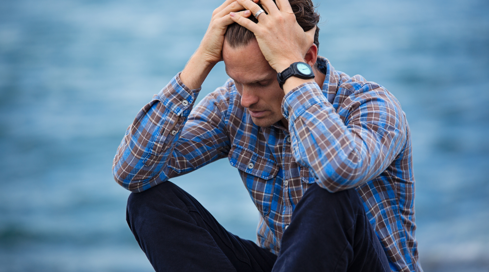 A man is sitting on the beach with his hands on his head.