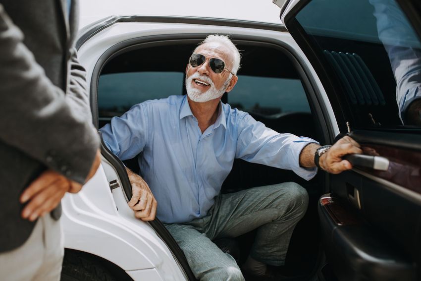 Smiling man with sunglasses stepping out of a white car, holding the door open
