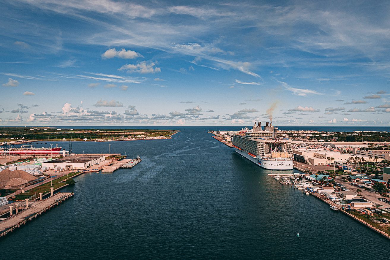 Aerial view of a wide canal with a cruise ship, flanked by port buildings under a blue sky.