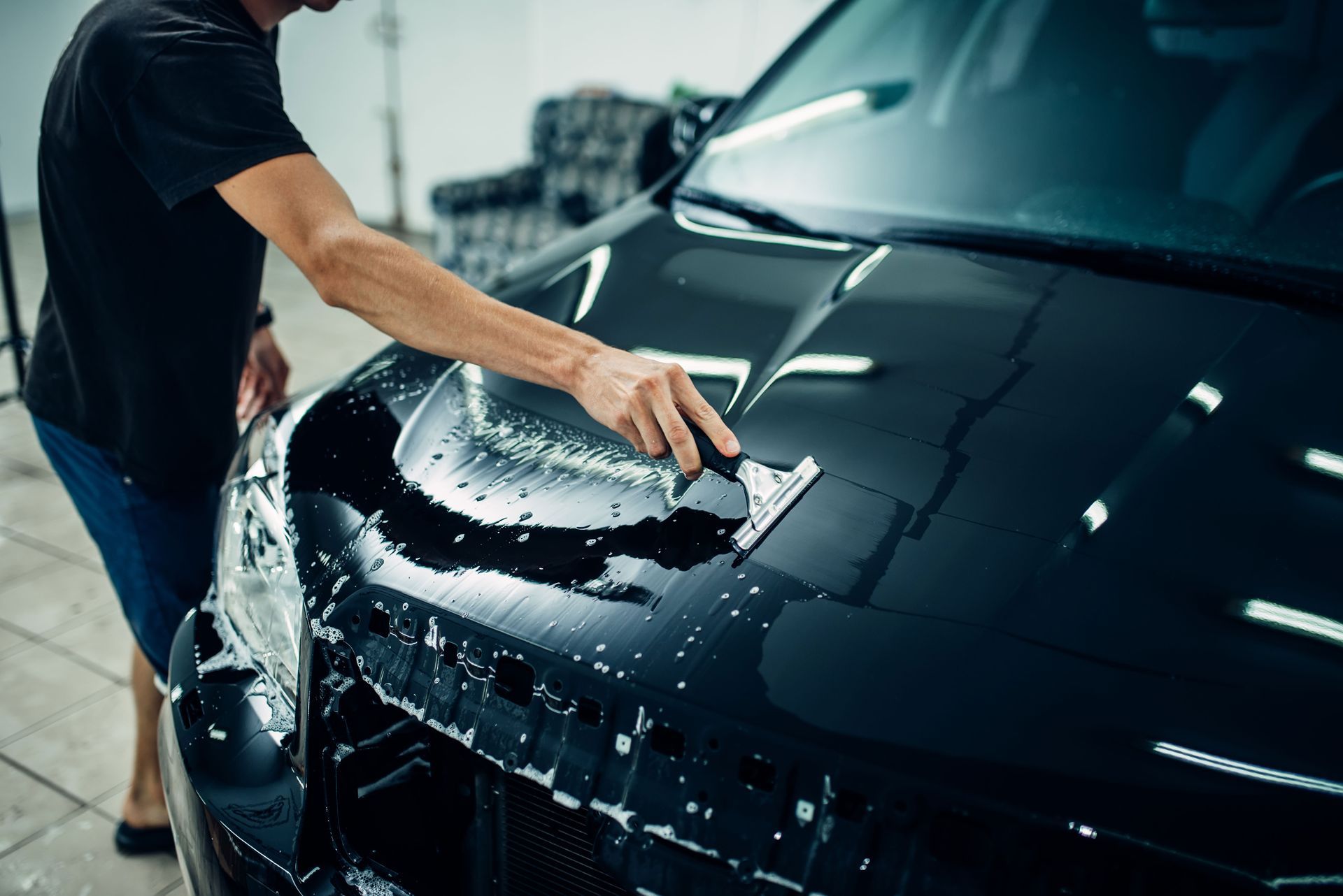 Person washing a black car hood with a sponge in a car wash.