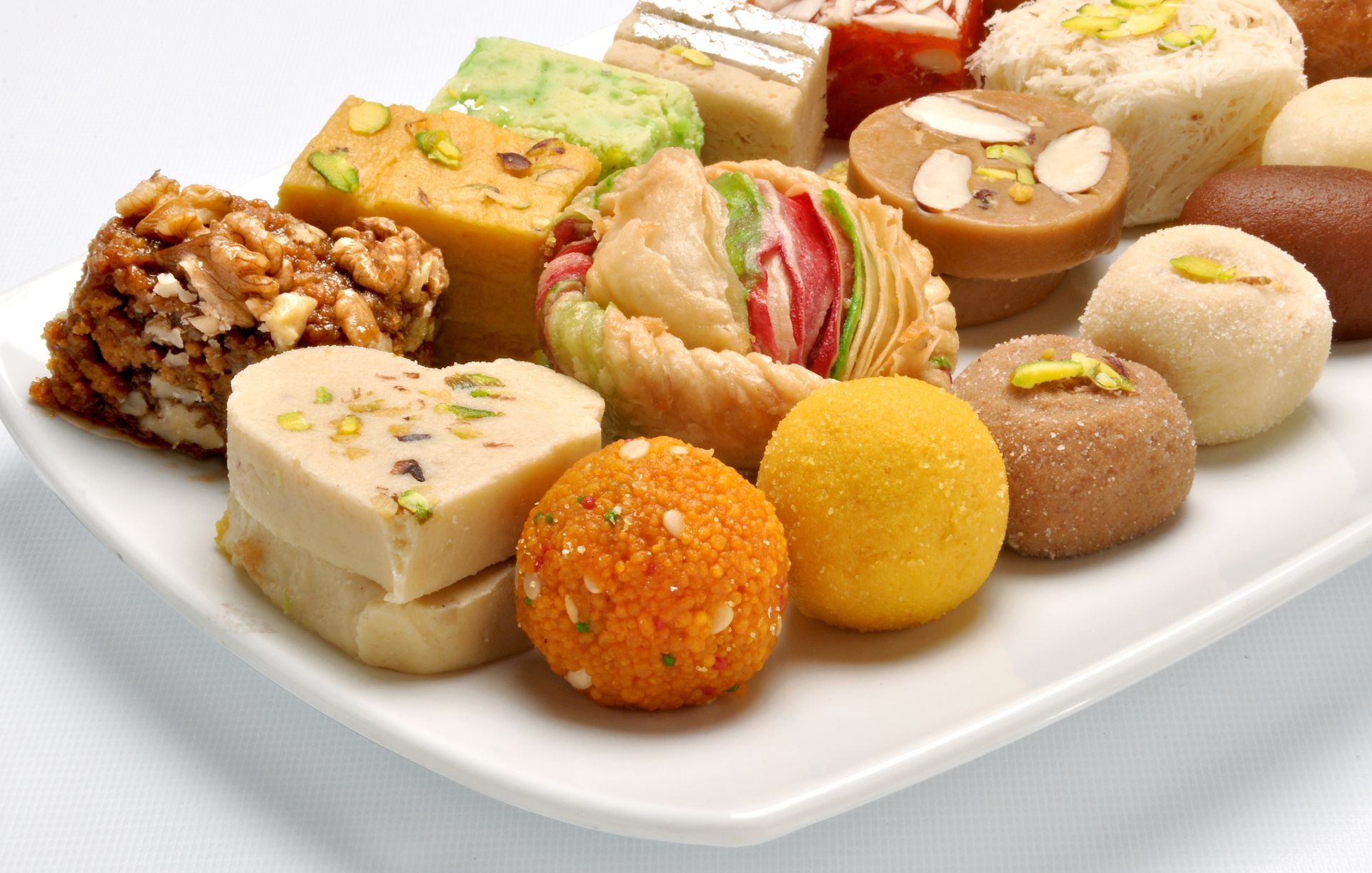 Un piatto bianco sormontato da una varietà di dolci indiani