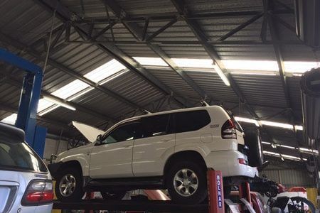 White Suv is Sitting on Top of a Lift in a Garage — Oaks Automotive Pty Ltd in Oak Flats, NSW
