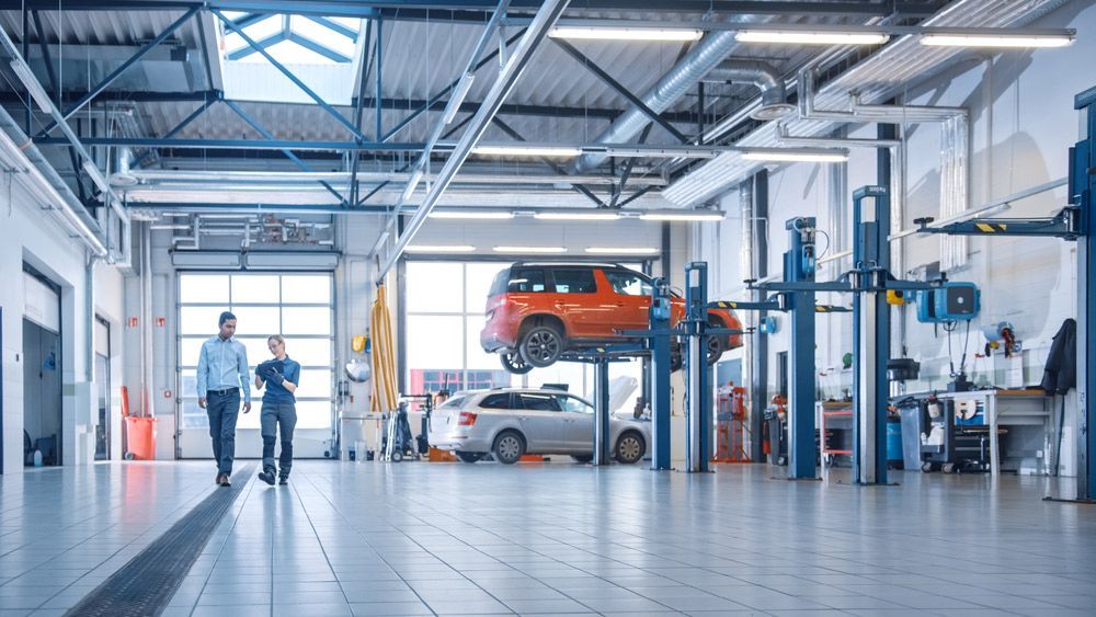 Two Men Are Walking in a Garage With a Car on a Lift — Oaks Automotive Pty Ltd in Oak Flats, NSW