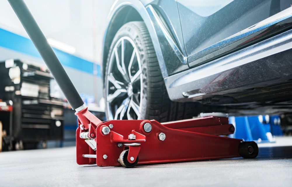 Car is Sitting on Top of a Red Floor Jack in a Garage — Oaks Automotive Pty Ltd in Oak Flats, NSW
