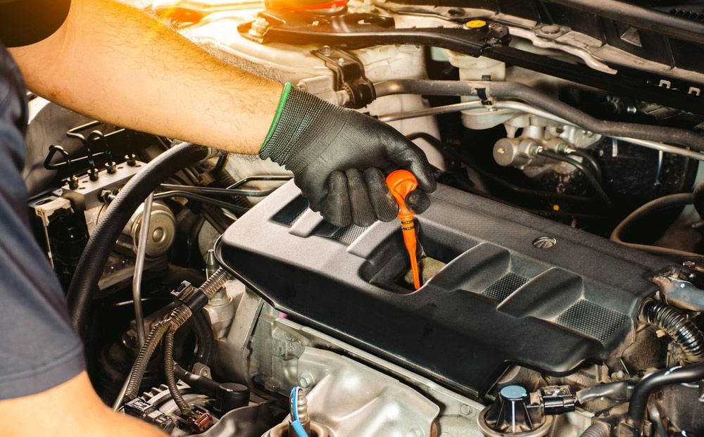 Man is Checking the Oil of a Car With a Dipstick — Oaks Automotive Pty Ltd in Oak Flats, NSW