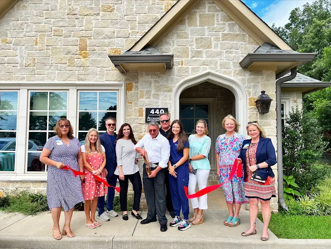 A group of people holding a red ribbon during a building grand opening ceremony in front of a stone exterior storefront.