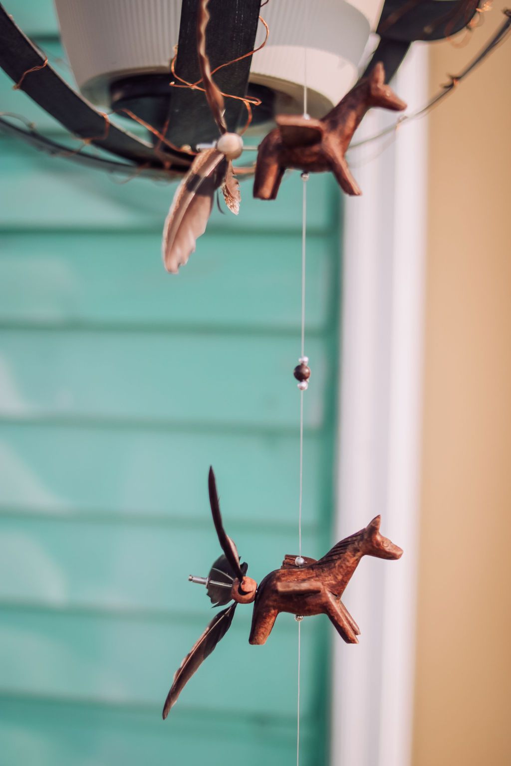 Wooden horse mobile with bird-like accents, hanging against a turquoise wall and tan trim.
