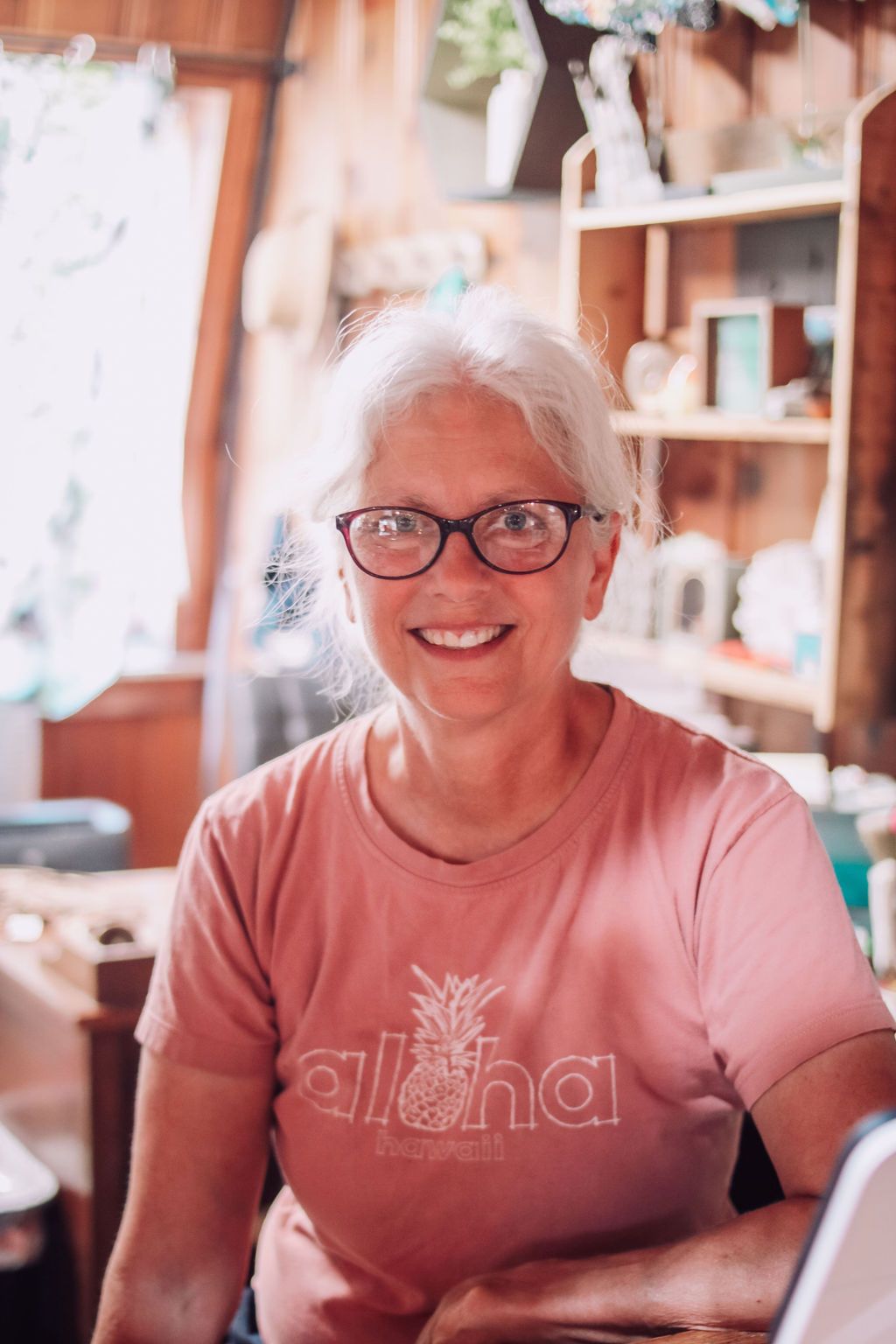 Woman with glasses smiles, wearing pink shirt with 
