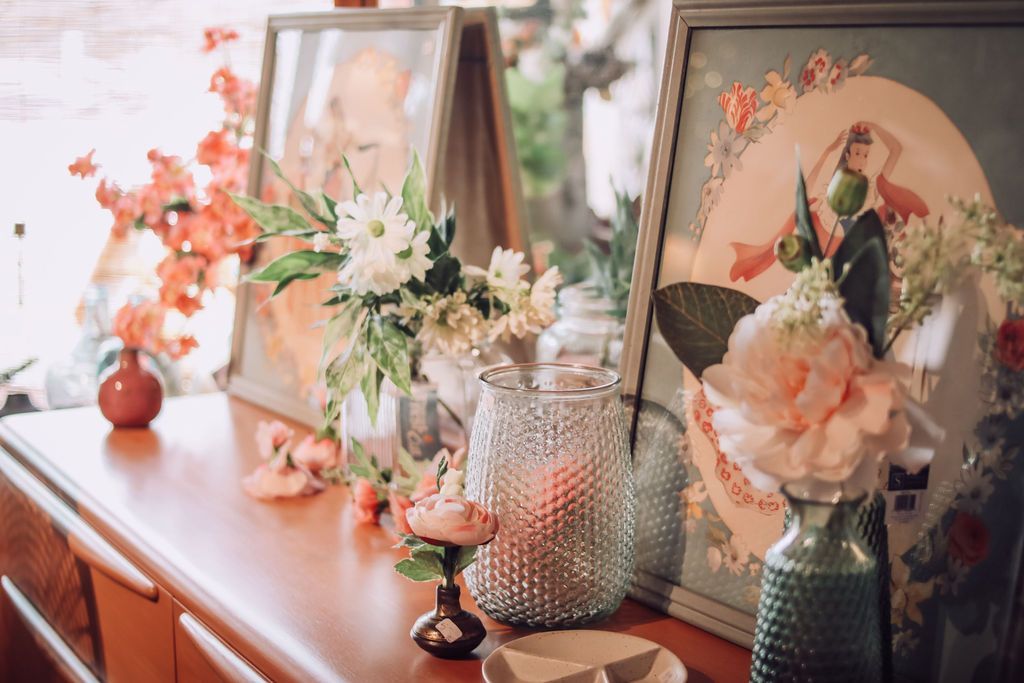 Wooden cabinet with framed art and vases of flowers in a brightly lit room.