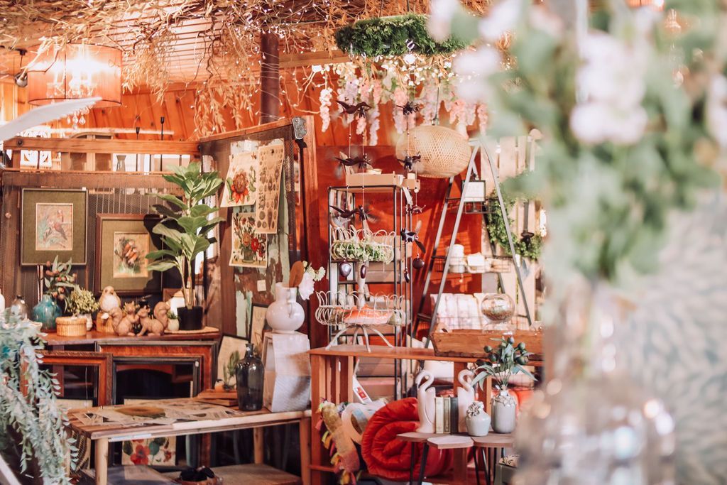 Eclectic shop interior with plants, furniture, and decorative items; warm lighting.