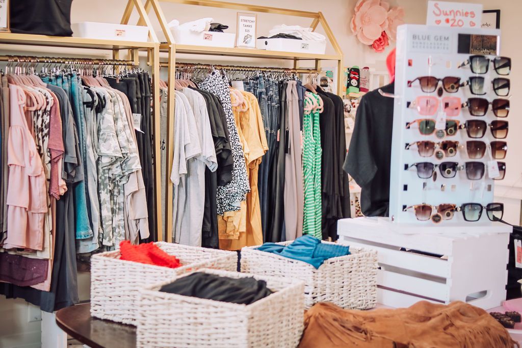 Clothing store interior with racks of clothes, sunglasses display, and wicker baskets.