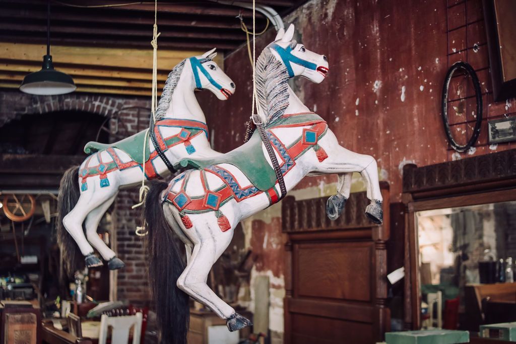 Two antique carousel horses hang from the ceiling, inside a room with peeling red walls.