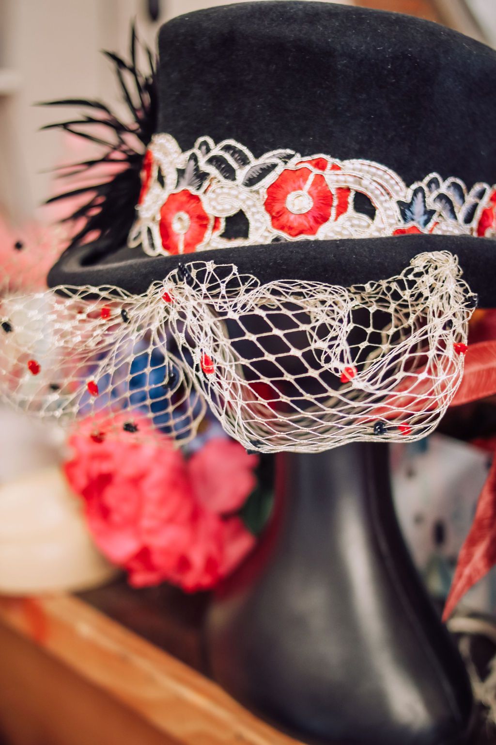 Black hat with red and white floral trim and a mesh veil, on a mannequin.