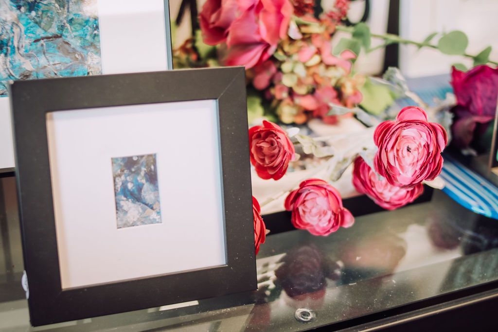 Black framed artwork with white mat, next to red roses.