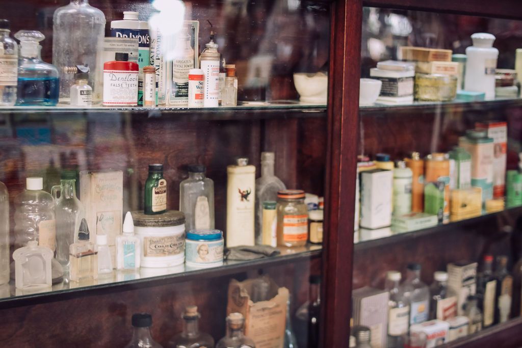 A wooden pharmacy cabinet filled with various antique medicine bottles and jars.