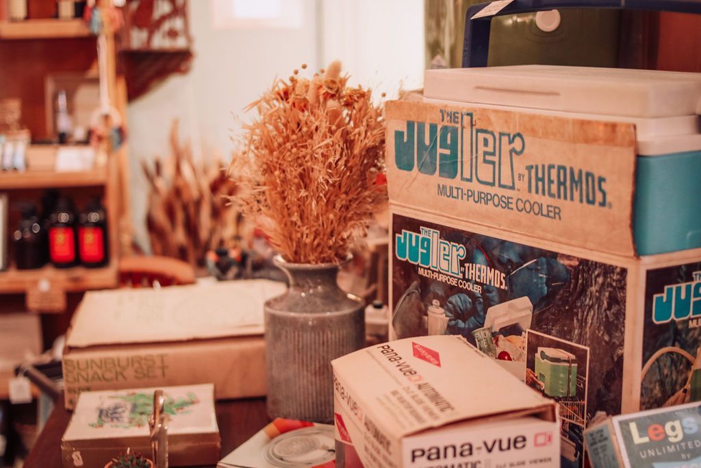 Vintage cooler box and dry flowers on a table in a shop with other items.