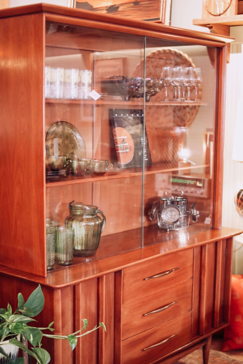 Mid-century modern wooden hutch with glass doors. Displaying glassware and a vintage radio.